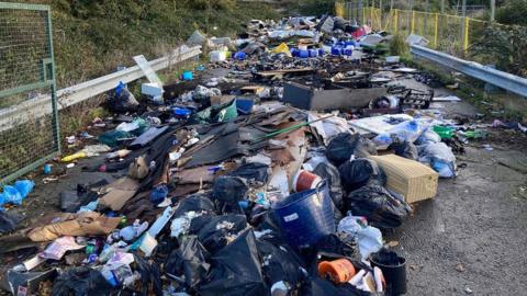 Rubbish dumped on a lane in Bristol. The image shows a variety of discarded items such as bags of rubbish, broken furniture and plastic waste. It stretches for many yards, from just in front of the camera into the distance