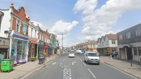 Gloucester Road in Bristol. Shops can be seen along either side of the street and cars are in the road. 