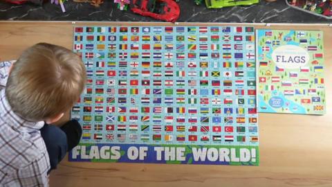 A boy crouching over a poster filled with colourful flags that reads 'Flags of the world!'