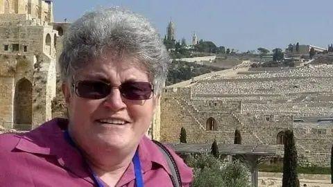 A woman wearing a pink shirt and sunglasses standing outside an ancient site.
