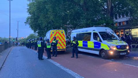 Police vans and officers standing in a bus lane on a road