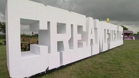 The word Creamfields is spelt out in giant white letters on the festival site, with grass and picnic benches and a stall visible.