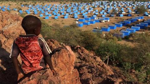 A boy sits atop a hill overlooking a refugee camp near the Chad-Sudan border, November 9, 2023