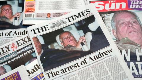 Several UK newspapers spread out showing front pictures of Andrew Mountbatten-Windsor photographed leaving a police station after his arrest