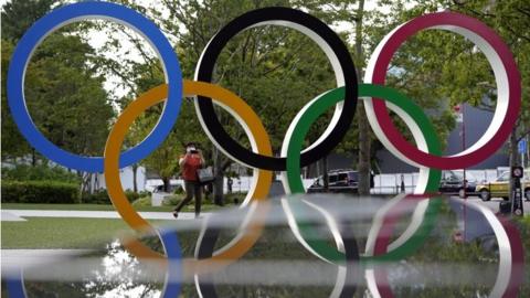 A woman in a face mask takes pictures of an Olympic Rings monument near the main venue for the Tokyo Olympics and Paralympics