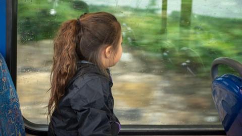 Girl looks out a window on a bus