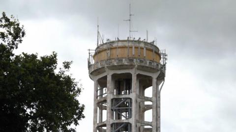 A close-up of the top of the Trimley St Mary water tower - a large concrete and steel tower with telecommunication equipment on top. 