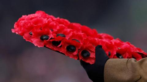 A close-up of a gloved hand holding a poppy wreath