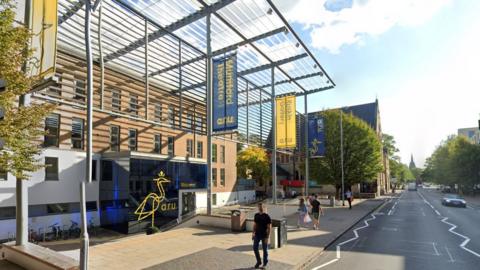 Building with ARU logos and flags in front with people walking past