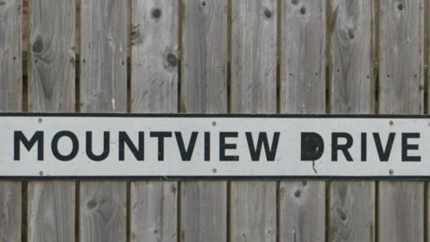 A road sign is attached to a wooden fence. It reads Mountview Drive in black writing on a white background