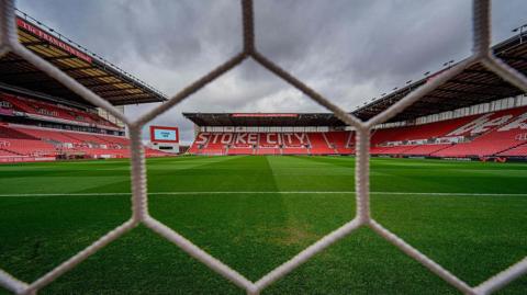 A general view, from behind the goal, of Stoke City's bet365 Stadium, with the goal netting in the foreground and three stands full of red seats in the landscape