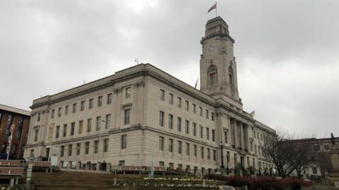 A cream-coloured town hall building surrounded by gardens.