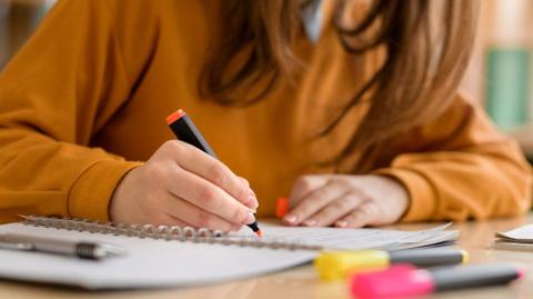 A school student annotating a notebook at a desk
