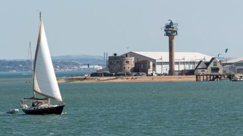 Sailing boat passing Calshot Activities center on the shores of the Solent, Calshot Spit, Southampton, England UK