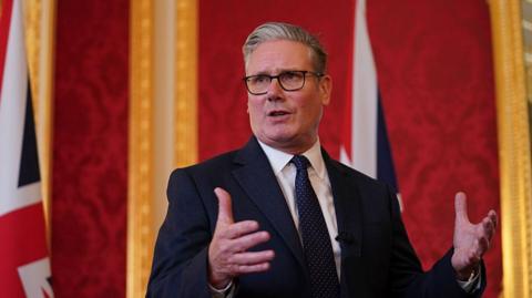 UK Prime Minister Keir Starmer speaking as he stands in front of two union jack flags.