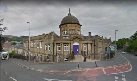 An old, grand-looking brick building with a bright purple door stands on a street corner. It has a domed roof in the middle.