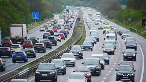 Cars queuing in both directions on the M5 motorway near Burnham-on-Sea in Somerset. There are trees either side of the motorway.