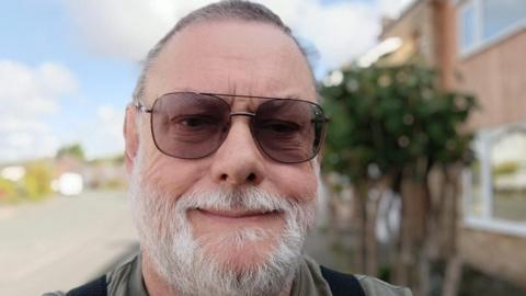 Image of John Crouchley, who is wearing sunglasses and has a grey beard.