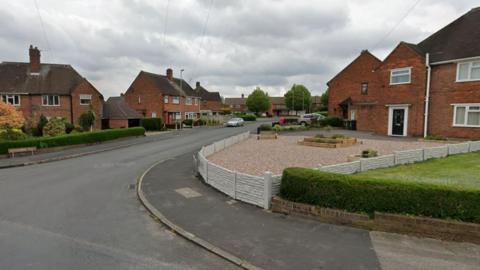 A google street image of a street with houses on both sides. A brown road sign saying Montgomery Road can be seen on a street corner. ON the right is a large front garden filled with stones and areas of bedding plants. Low hedges demarcate other garden boundaries with the pavement.