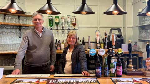 Andrew Joyce (left) and Dianne Cannon (right) stood behind a bar.