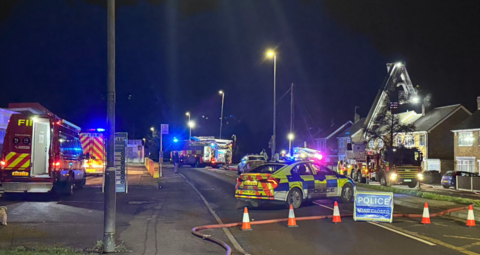 Several emergency service vehicles parked on a road at night with orange cones blocking the street.