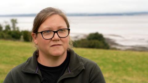A woman with black rimmed glasses and a brown fleece standing in a field