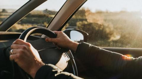 A stock image of a pair of hands on a car steering wheel