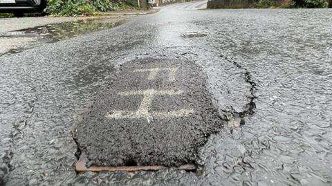 Manhole repair in road showing a patch of new tar 