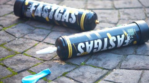Two discarded nitrous oxide cannisters on the ground alongside a deflated balloon.