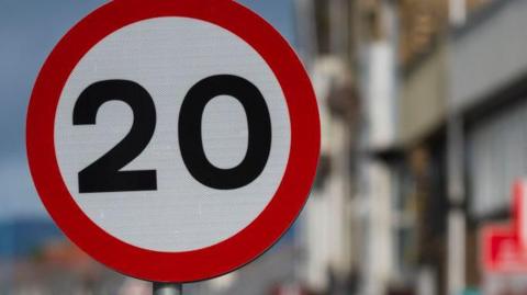 Picture of the 30mph road sign in a street. The background is heavily blurred. 