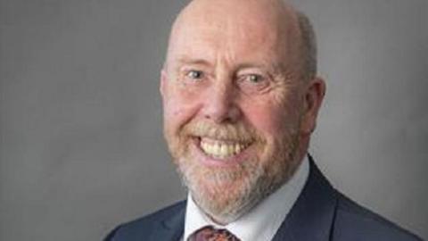 Headshot of Reg Kain looking at the camera and smiling. He is wearing a suit and tie. 