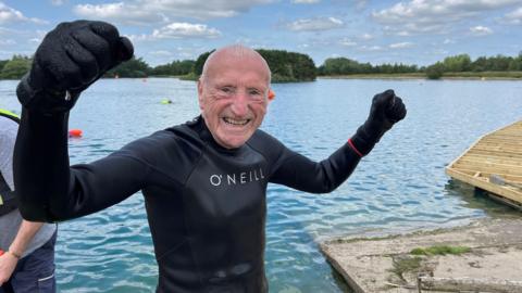 David stands with fists raised in the air with the lake behind him 