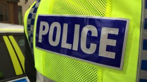 Close up of an officer wearing a high vis vest with 'police' written on the back