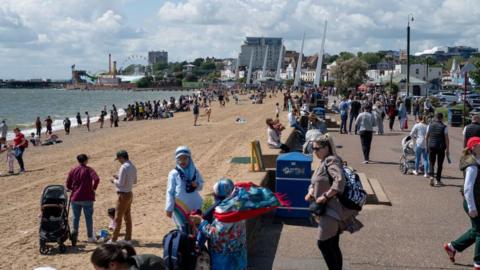 Crowds of people are on the beach and walking along a pavement at Southend seafront.