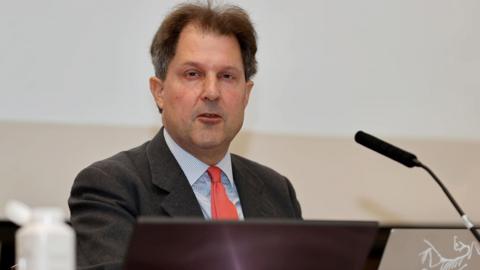 Angus McCullough KC has dark short hair and is sitting behind a microphone.
He is wearing a grey suit, pale blue shirt and red tie.

