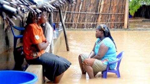 Neighbours chat while sitting in a flooded street of the Paquite district of Pemba