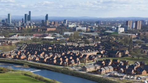 The Greater Manchester skyline, with tower blocks and skyscrapers in the background and an estate of brick-built houses in the foreground