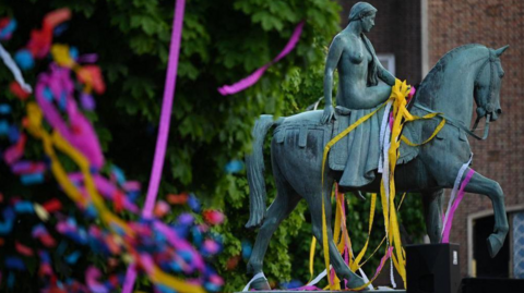 The green statue of Godiva in Coventry, with colourful paper streamers draped over
