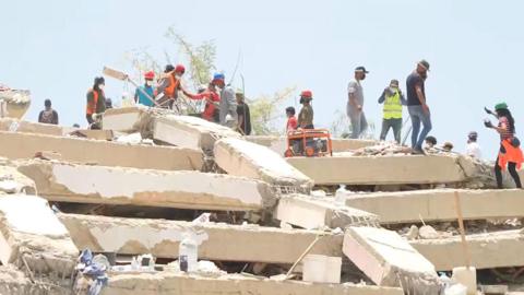 A landscape image of people conducting a search on top of a mass of rubble from collapsed buildings