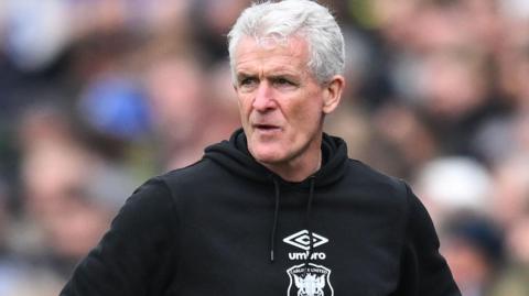 Mark Hughes, wearing a Carlisle hoodie, watching his team play last season