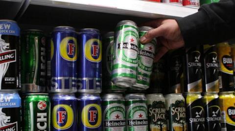 The alcohol aisle of a shop, with shelves stocked with canned beers, ciders and alcoholic drinks.