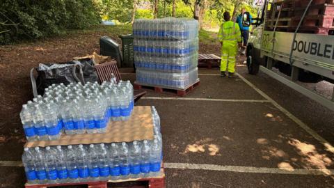Several slabs of water placed at a car park. There is a contractor, in a hi-vis clothing, standing beside a lorry. 