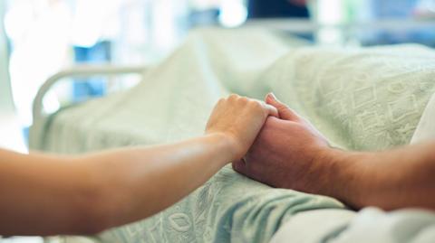A woman hold's a patient's hand in a hospital bed