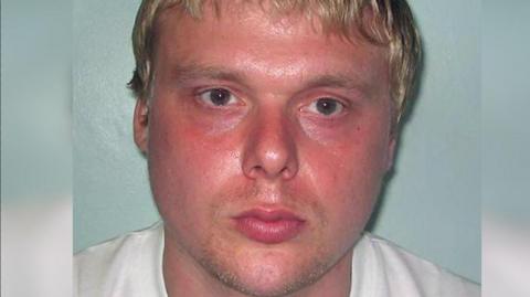 Steven Barker police mugshot image. He looks towards the camera and has a sweaty pink face, blond hair and is unshaven