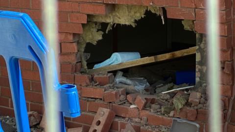 A close‑up of a hole in a brick wall showing broken bricks and debris.
