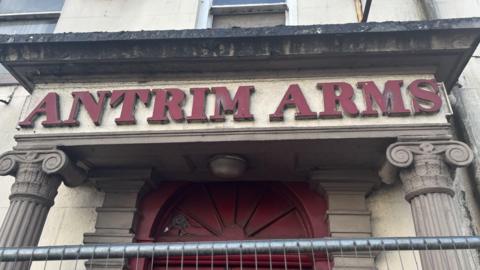 ANTRIM ARMS above a red door way. The lettering is also red.