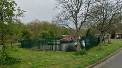 A car park next to a residential road with trees and grass all around.