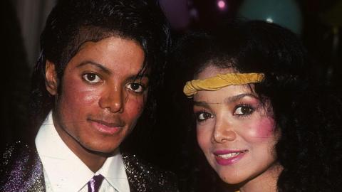 Michael Jackson in a white shirt, dark sparkly tie and dark sparkly jacket, next to La Toya Jackson who is wearing a yellow headband. 