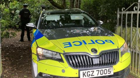 It shows a police car with PSNI crest and two policemen standing with their backs to the camera