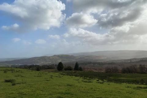 Rolling hills stretch into the distance under a partly cloudy sky, with patches of sunlight and mist creating a soft, hazy atmosphere.
